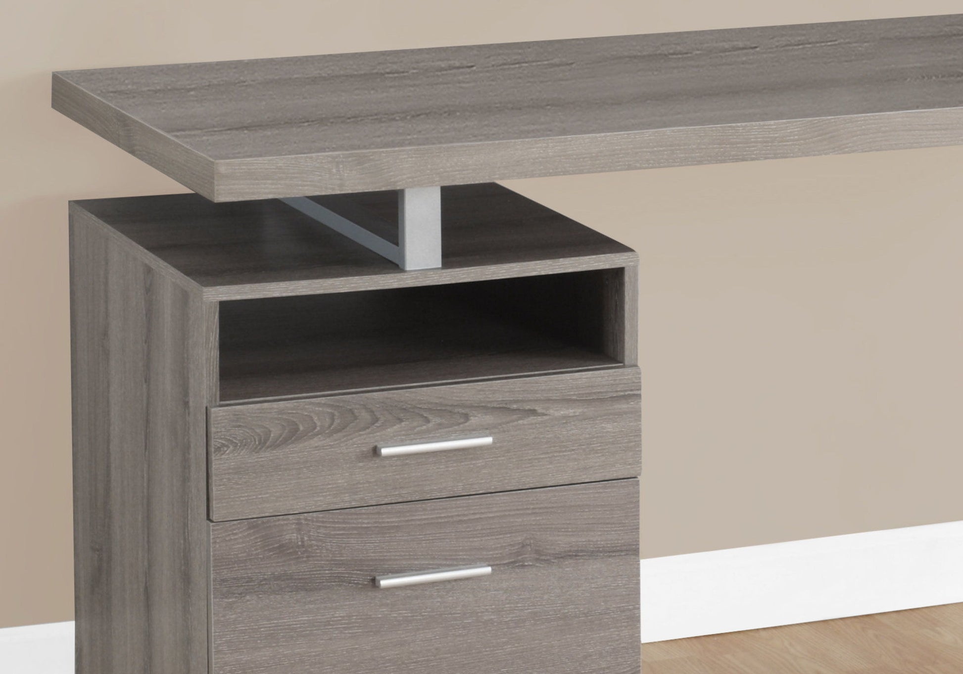 A close-up of the Computer Desk For Home Office, Laptop, Left Right Set-Up with a grey finish, featuring one open shelf, two storage drawers with silver handles, and a rectangular tabletop supported by a metal bracket against a beige wall.
