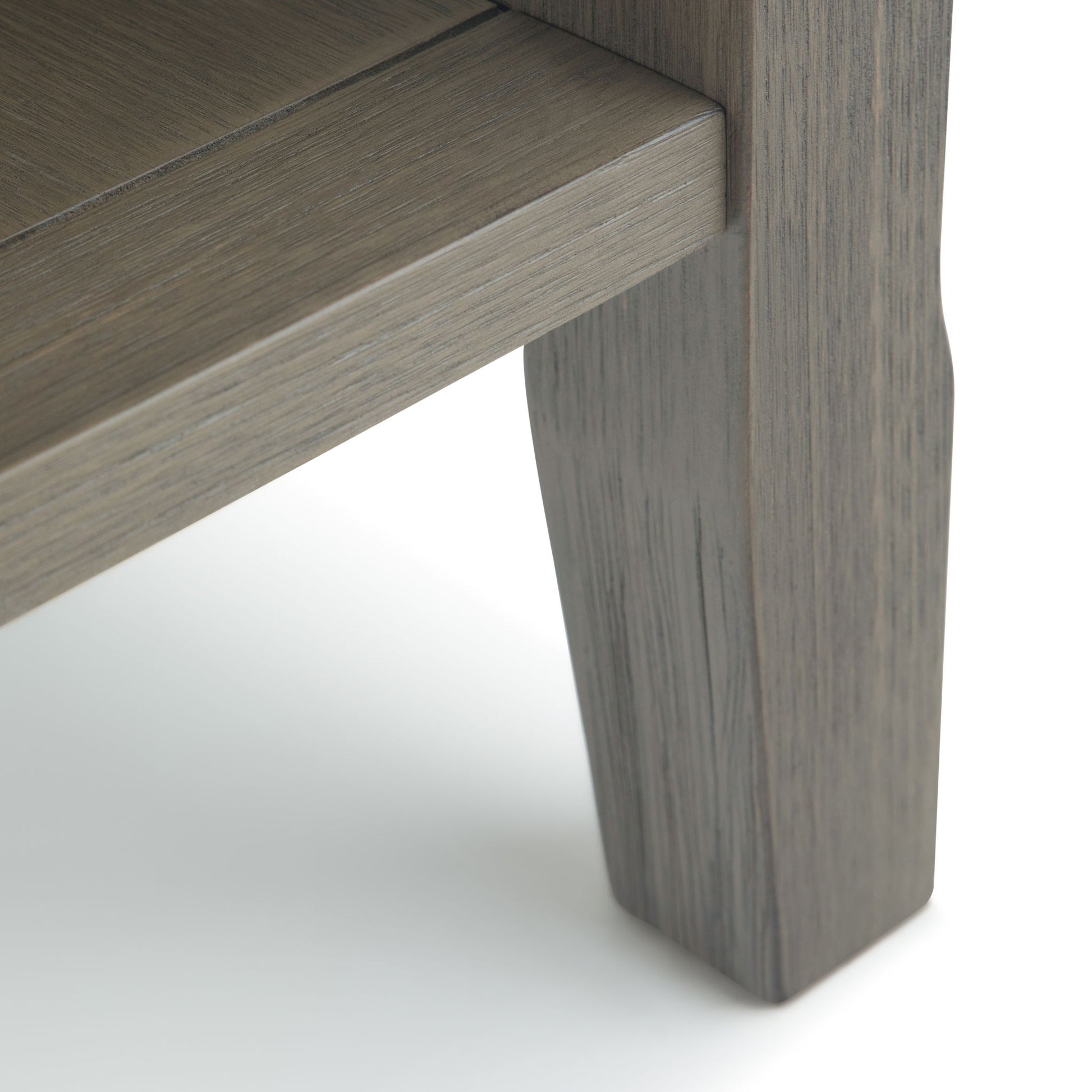 Close-up of the Acadian - Narrow Side Table, Handcrafted, featuring a grey-brown finish on its corner leg that highlights the wood grain and smooth texture against a white background.