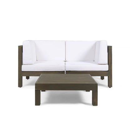 The Oana 3 Piece Love Seat Set features a modern outdoor sofa with white cushions and a dark wooden frame, paired with a matching low rectangular coffee table, all displayed against a plain white background.