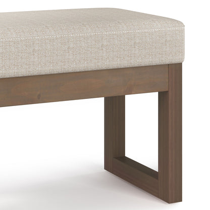 The Milltown Upholstered Ottoman Bench features a light beige cushion and a wooden base with simple rectangular legs, offering a modern, minimalist design.