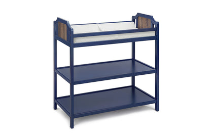 The Brees - Changing Table is navy blue wood, features two lower storage shelves, white cushioned changing pad on top, and wood accent panels at each end.