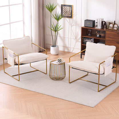 Two Upholstered Hanging Armchairs with gold-plated metal frames, crushed foam cushions, and skin-friendly fabric sit on a light rug by a round table with a chessboard. A tall plant and bookshelf decor are near large curtained windows in the background.
