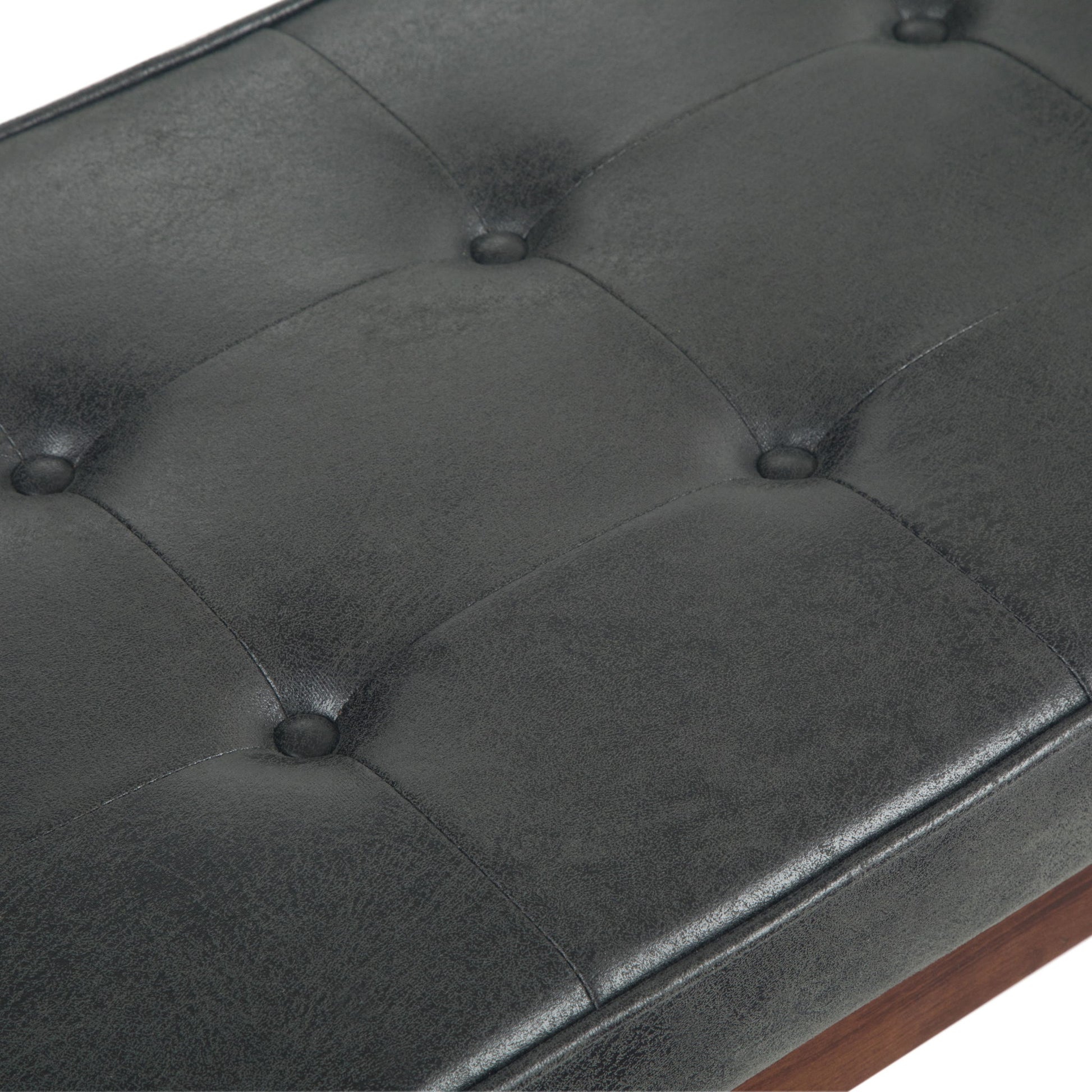 Close-up of the Pierce Mid Century Upholstered Ottoman Bench in black tufted leather or faux leather with button detailing and visible stitching, set on a wooden frame.