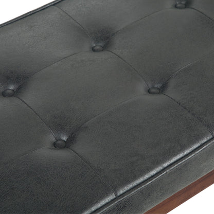 Close-up of the Pierce Mid Century Upholstered Ottoman Bench in black tufted leather or faux leather with button detailing and visible stitching, set on a wooden frame.