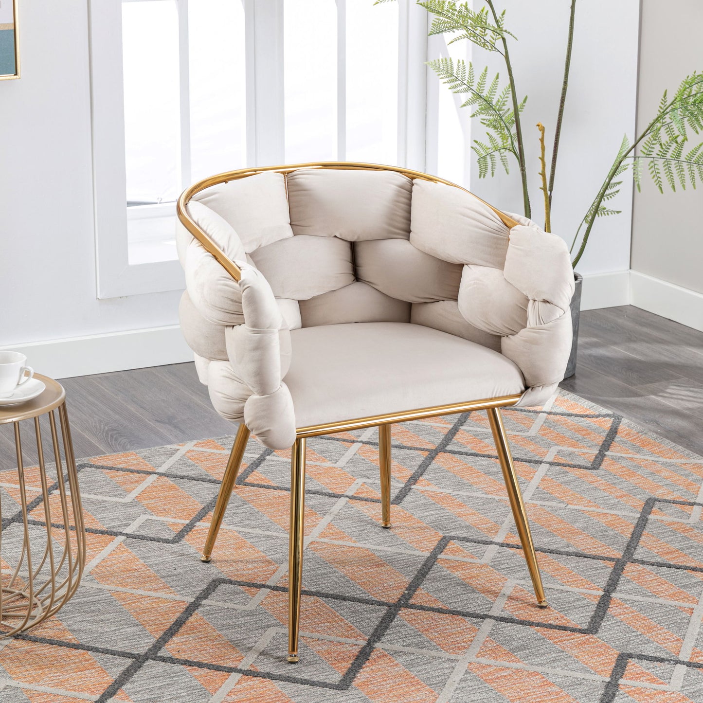 The Luxury Modern Simple Leisure Velvet Single Sofa Chair with gold legs and a tufted cream cushion is placed on a patterned rug beside a side table and potted plant in a bright, modern room.