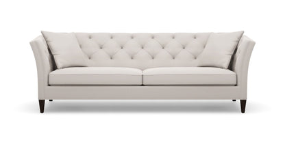 Introducing the Shelton 98" Sofa: a cream-colored masterpiece with a contemporary flair, featuring a tufted backrest and two perfectly matching throw pillows. The design boasts sleek, slightly flared arms complemented by elegant wooden legs, all showcased against a plain white backdrop.