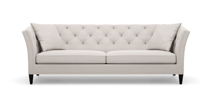 The Shelton 98" Sofa is a modern piece with a light grey finish, tufted design, and sloped arms paired with black legs. It includes two matching cushions, and its clean lines along with the neutral color contribute to its elegance and versatility in complementing various interior styles.