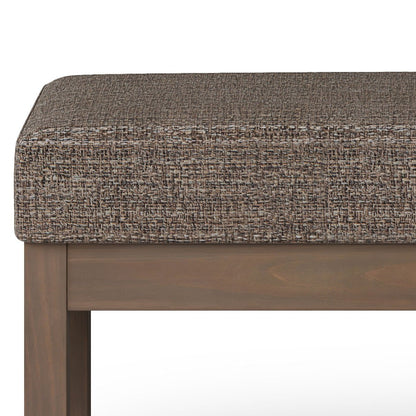 A close-up of the Milltown Upholstered Ottoman Bench, showcasing its textured brown cushion and wooden frame with straight legs and a rectangular design.