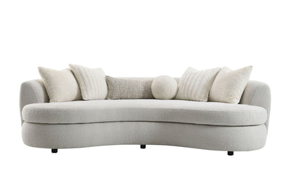 The Couch.com Iniko Boucle Sofa features a modern curved design in beige, comes with four large square and one round toss pillow, all in matching soft textured fabric, plus short black legs for a plush, cozy look and durable construction.