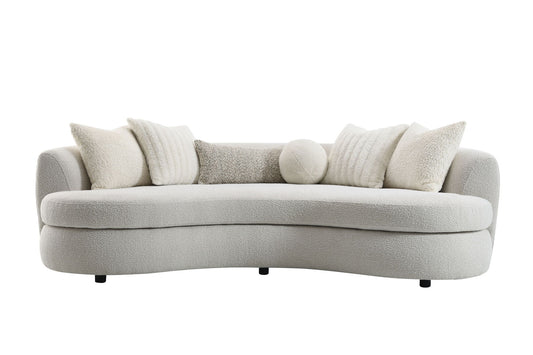 The Couch.com Iniko Boucle Sofa features a modern curved design in beige, comes with four large square and one round toss pillow, all in matching soft textured fabric, plus short black legs for a plush, cozy look and durable construction.