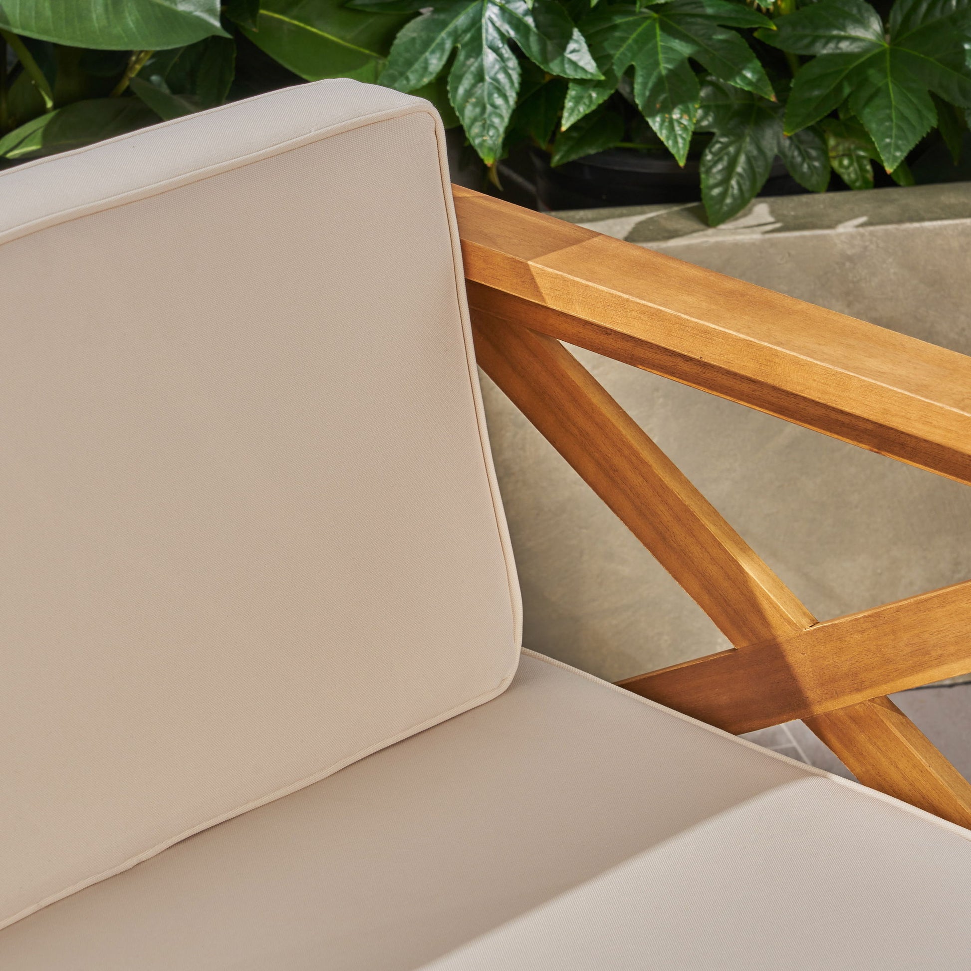 Close-up of the Alcove - L Shape Sofa Set, featuring beige cushions, a wooden armrest, and green leafy plants in the background.