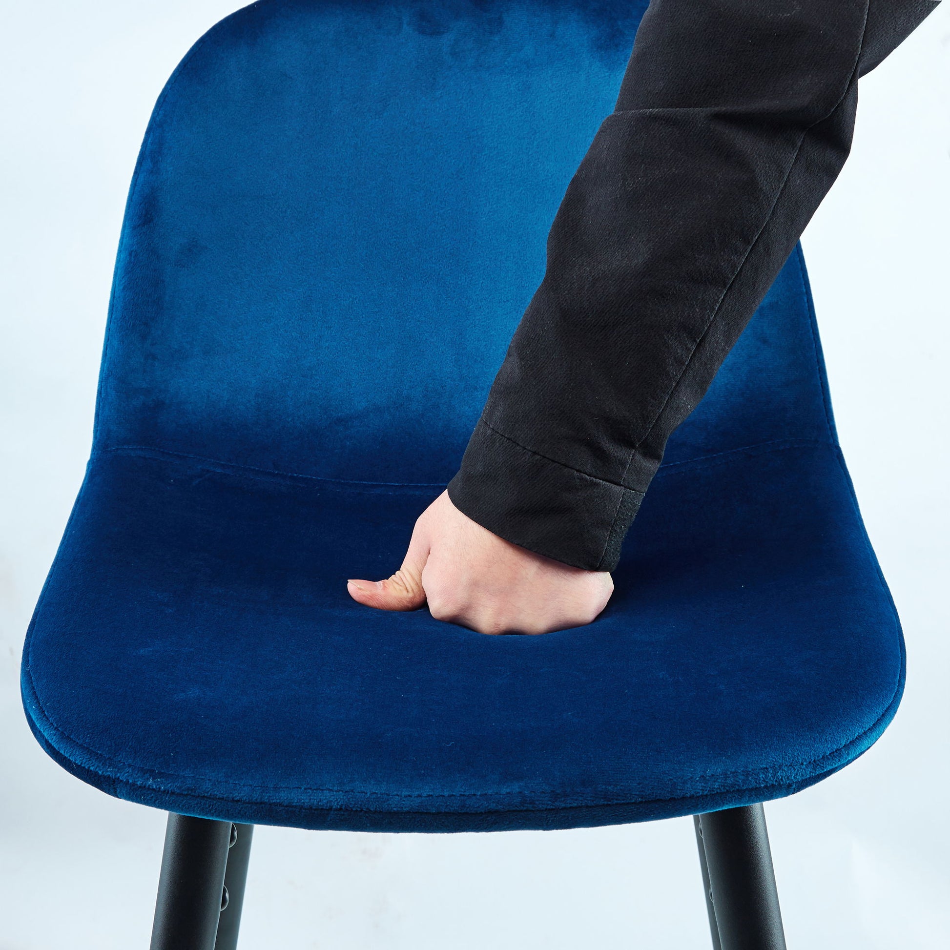 A person in a black sleeve presses their fist into the cushion of the Velvet Barstool With Back (Set of 2), showing its soft and comfortable blue velvet upholstery.