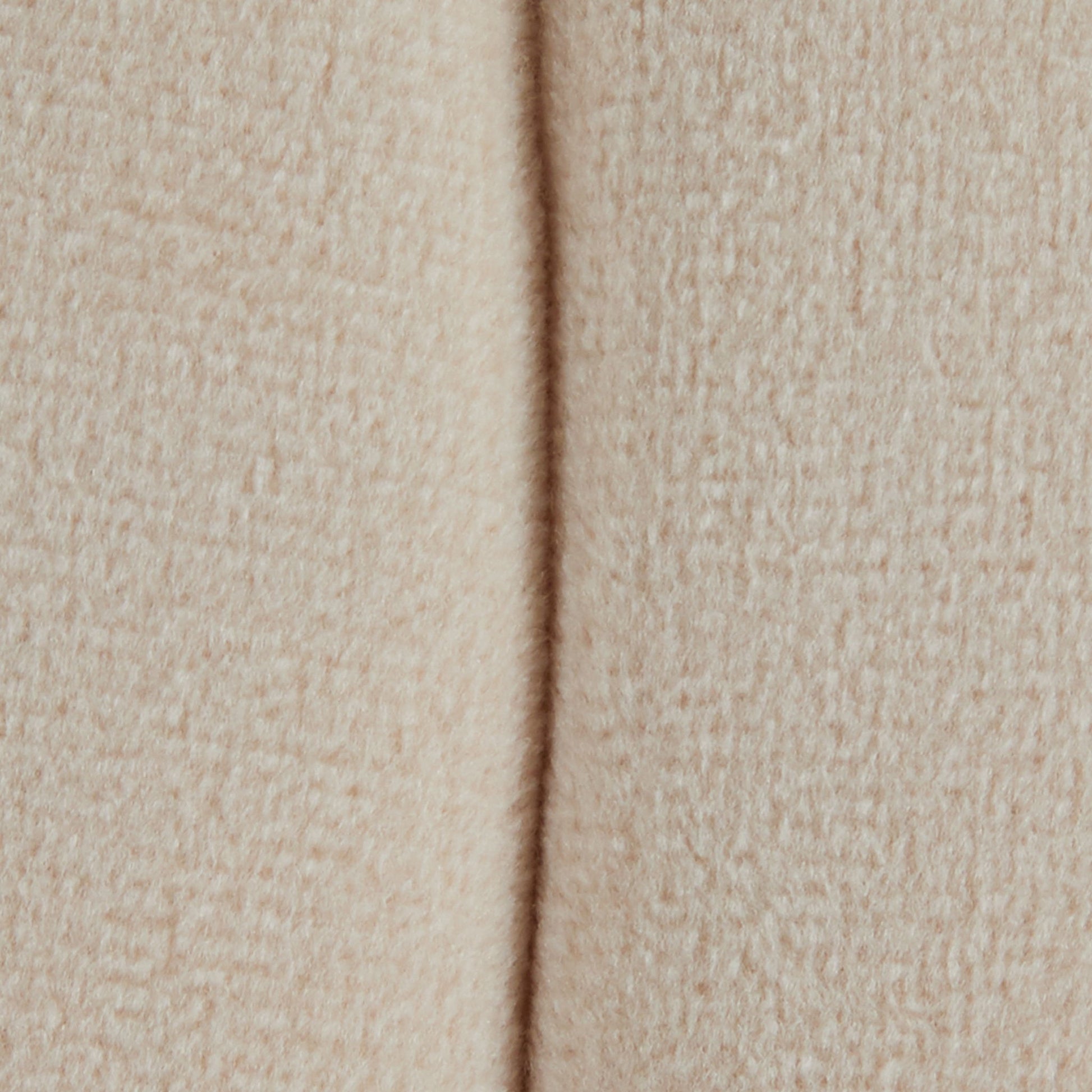 Close-up of the Braided - Versatile Round Ottoman shows its soft, beige, textured fabric with a vertical seam running down the center.