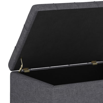 A close-up of the Harrison - Upholstered Coffee Table Storage Ottoman shows its gray fabric, open hinged lid, and spacious black interior. Modern brass hinges support the lid, combining style with practical storage.