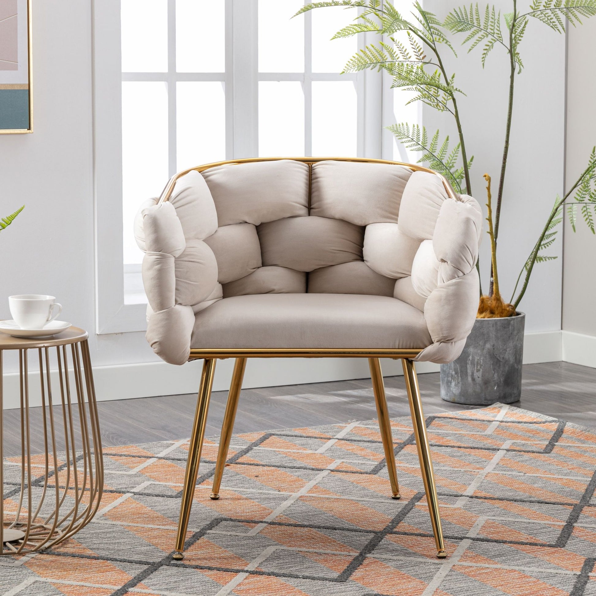 The Luxury Modern Simple Leisure Velvet Single Sofa Chair features a tufted light beige cushion and gold metal legs, perfect for bright rooms with large windows, alongside a side table, patterned rug, and potted plants.