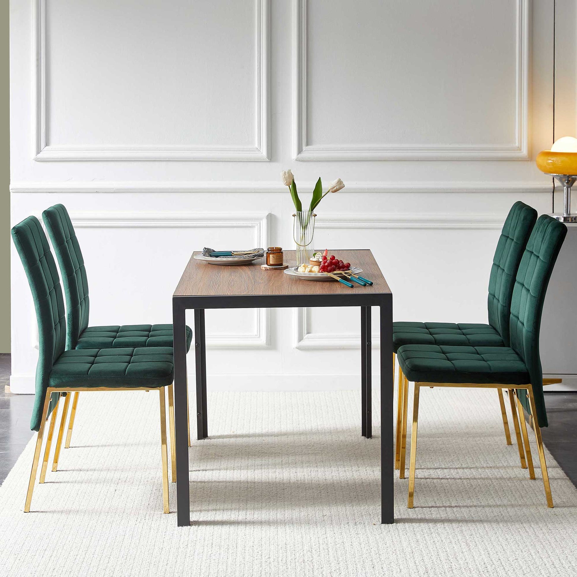 The 5 Pieces Dining Set includes velvet high-back Nordic dining chairs with golden legs and a creative design table, set for two with plates, utensils, a vase of white tulips, and fruit. Four green chairs flank the wooden table with black legs.