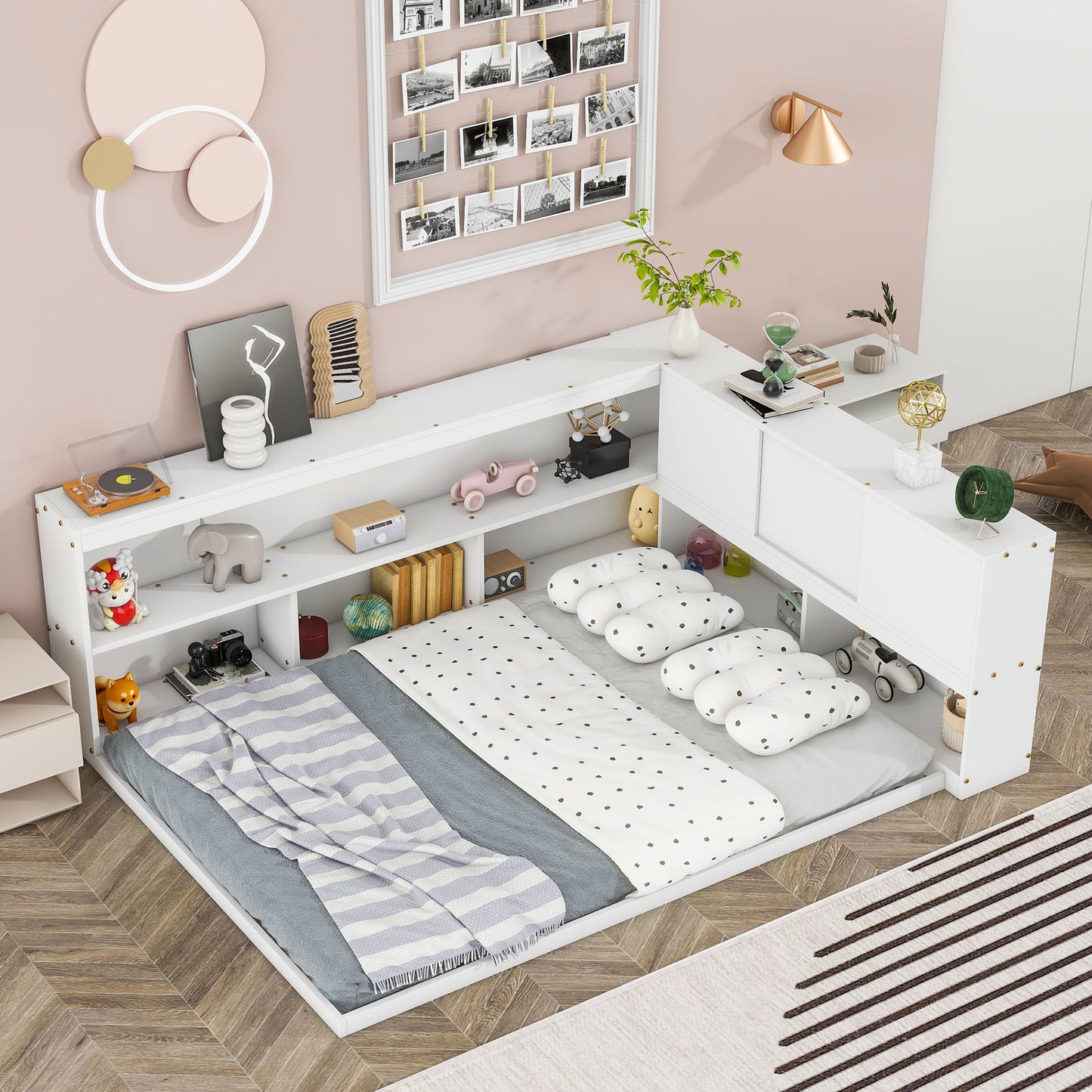 A cozy bedroom features the Floor Bed With L-Shaped Bookcases, Sliding Doors, Without Slats, styled with polka-dot pillows and a striped blanket. Pastel art, a photo collage, plants, and wooden flooring complete the warm look.
