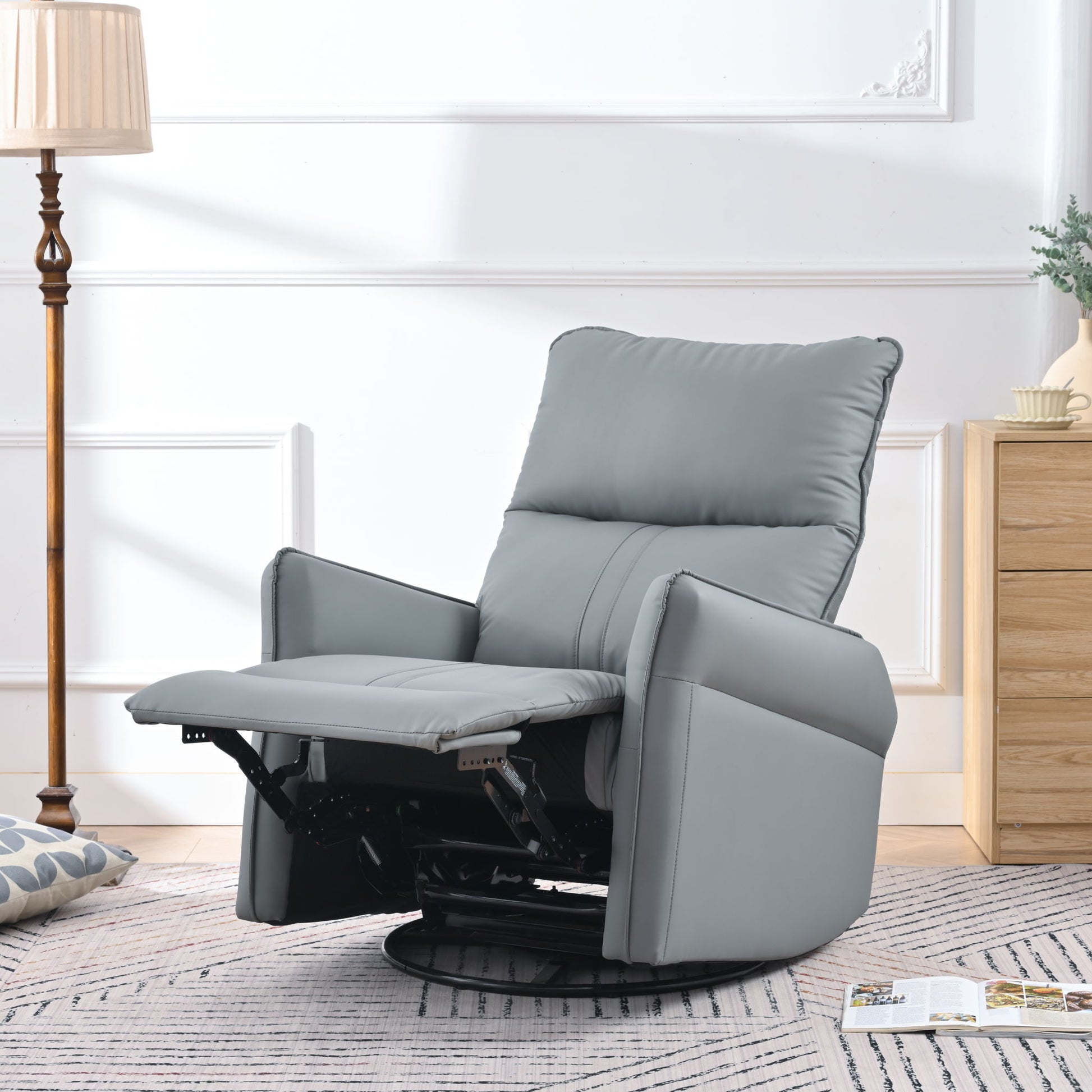 A 360° Modern Small Rocking Swivel Recliner Chair With Side Pocket in gray features an extended footrest and sits in a bright living room beside a wooden lamp, a bedside table with a plant, and a patterned floor cushion.