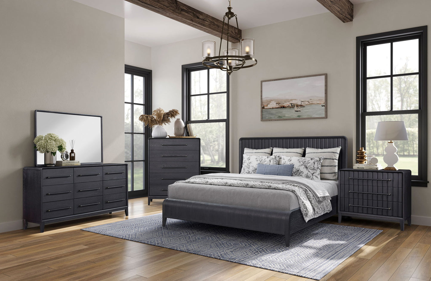 A modern bedroom features the Waterfall Panel Bed and matching black furniture—a dresser with mirror, tall chest, and nightstand. Large windows, wood floors, neutral walls, a chandelier, art, lamps, and plants create a bright, inviting atmosphere.