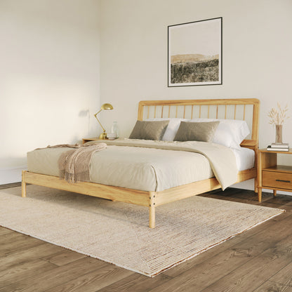 Minimalist bedroom featuring the Mid-Century Modern Solid Wood Spindle Bed with beige bedding, two pillows, a bedside table and lamp, decorative vase, wall art above the bed, all on a woven rug atop wooden flooring.