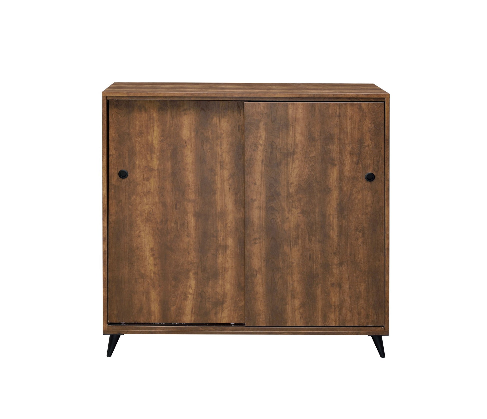 The Waina Shoe Cabinet in oak features a medium brown finish, two sliding doors with round black knobs, and four short black angled legs. Its simple, modern design makes it a stylish storage solution.