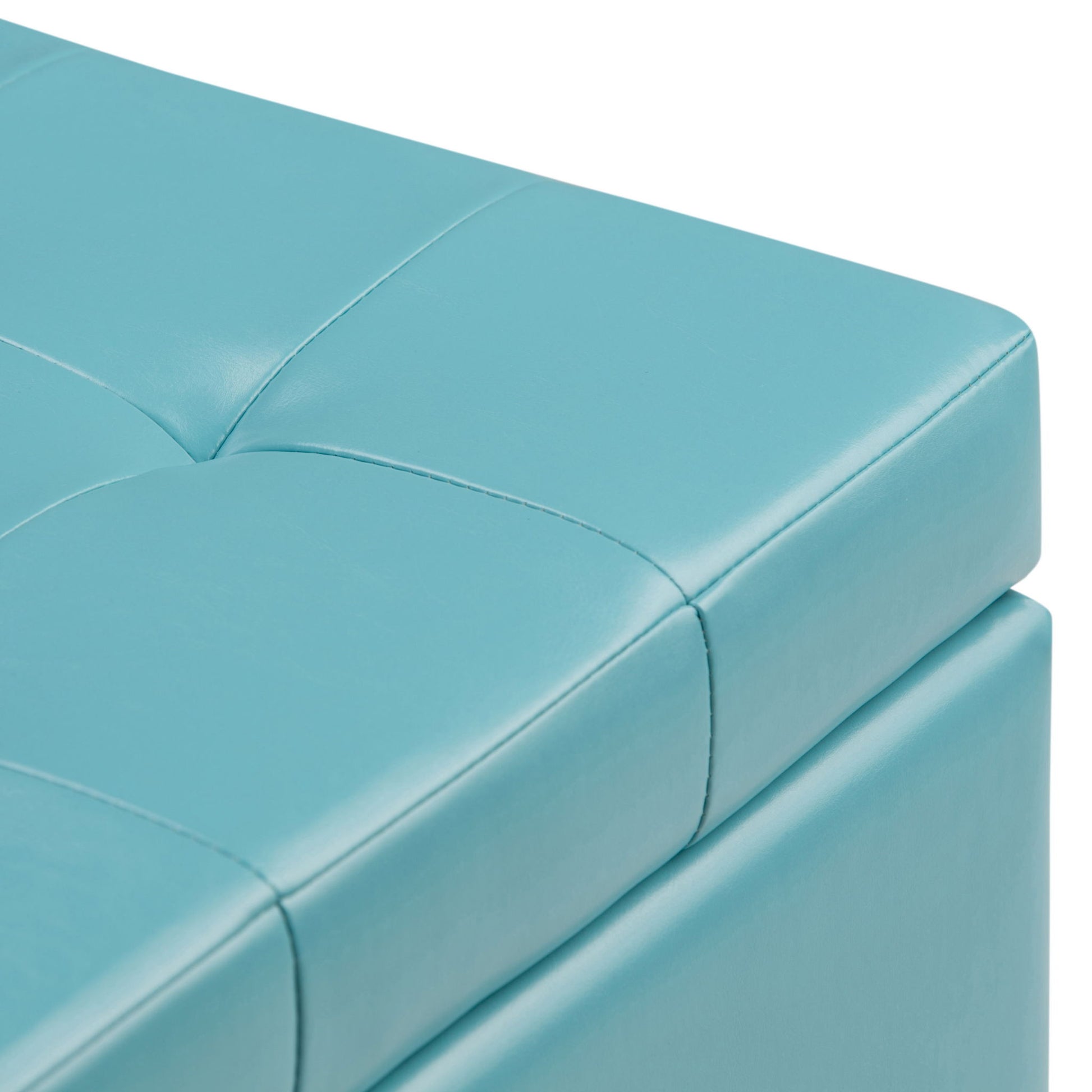 Close-up of the corner of the Cosmopolitan Upholstered Storage Ottoman in light blue faux leather, featuring tufted detailing, visible stitching, and cushioned upholstery.