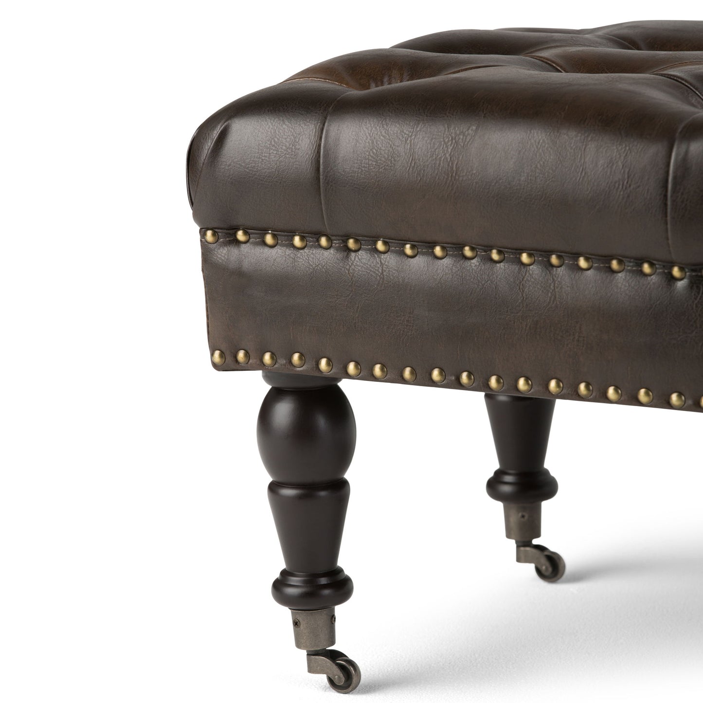 Close-up of the Henley Tufted Ottoman Bench in distressed brown leather, featuring brass nailhead trim, turned wooden legs, and small metal caster wheels, set against a white background.
