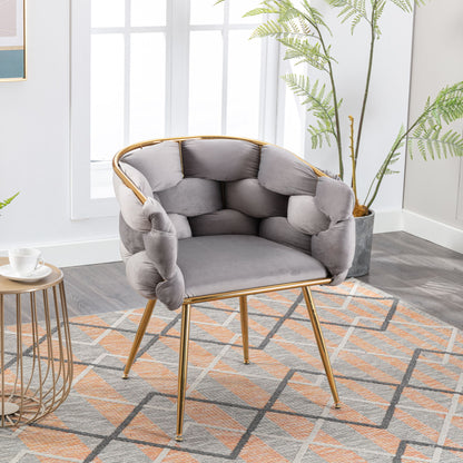 The Luxury Modern Simple Leisure Velvet Single Sofa Chair with a cushioned back and gold legs is placed on a geometric rug near a round side table in a bright room with large windows and green plants.