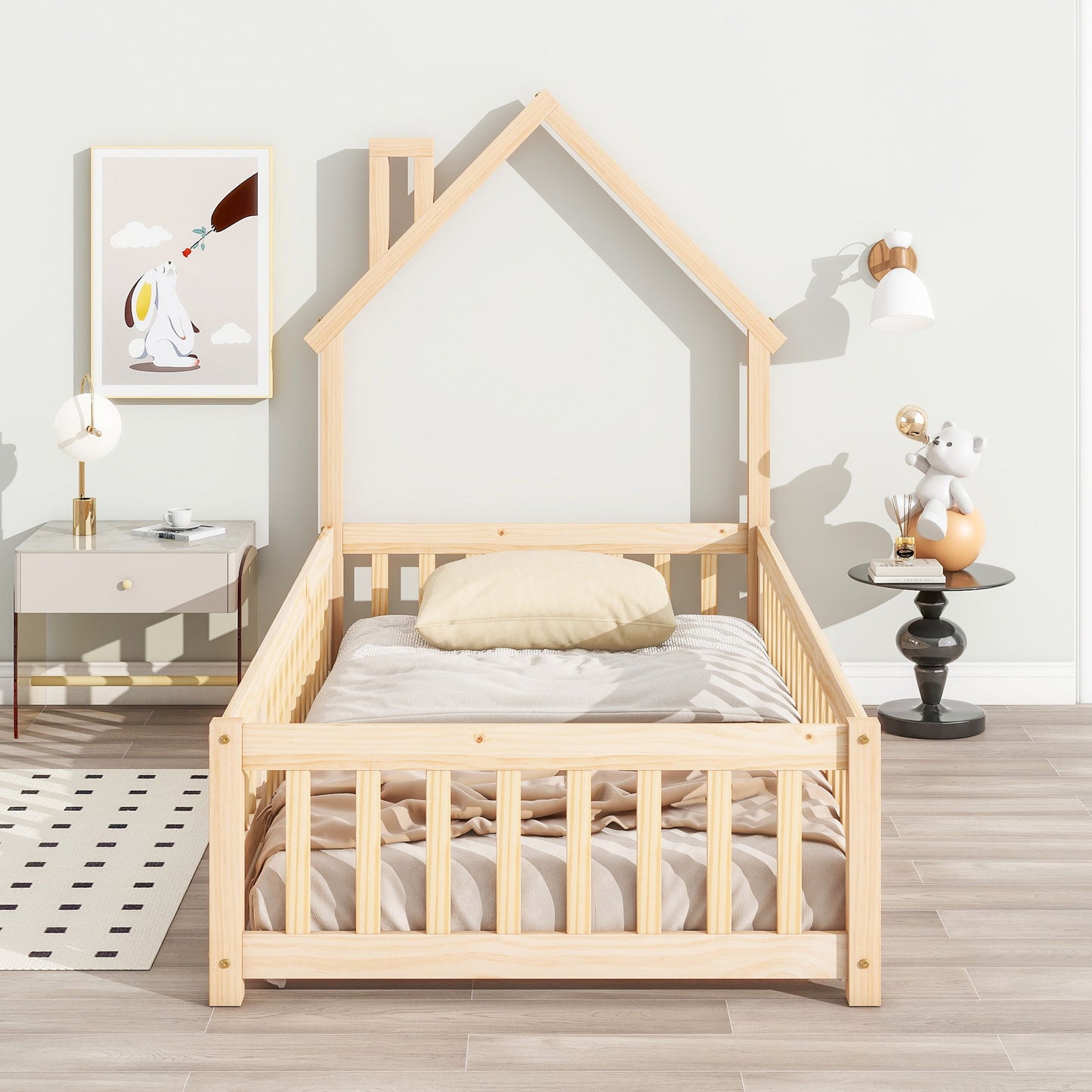 A House-Shaped Headboard Floor Bed With Fence with beige bedding sits in a bright room. To the left is a nightstand with a lamp beneath animal art; on the right, a small table holds a toy under a wall sconce.