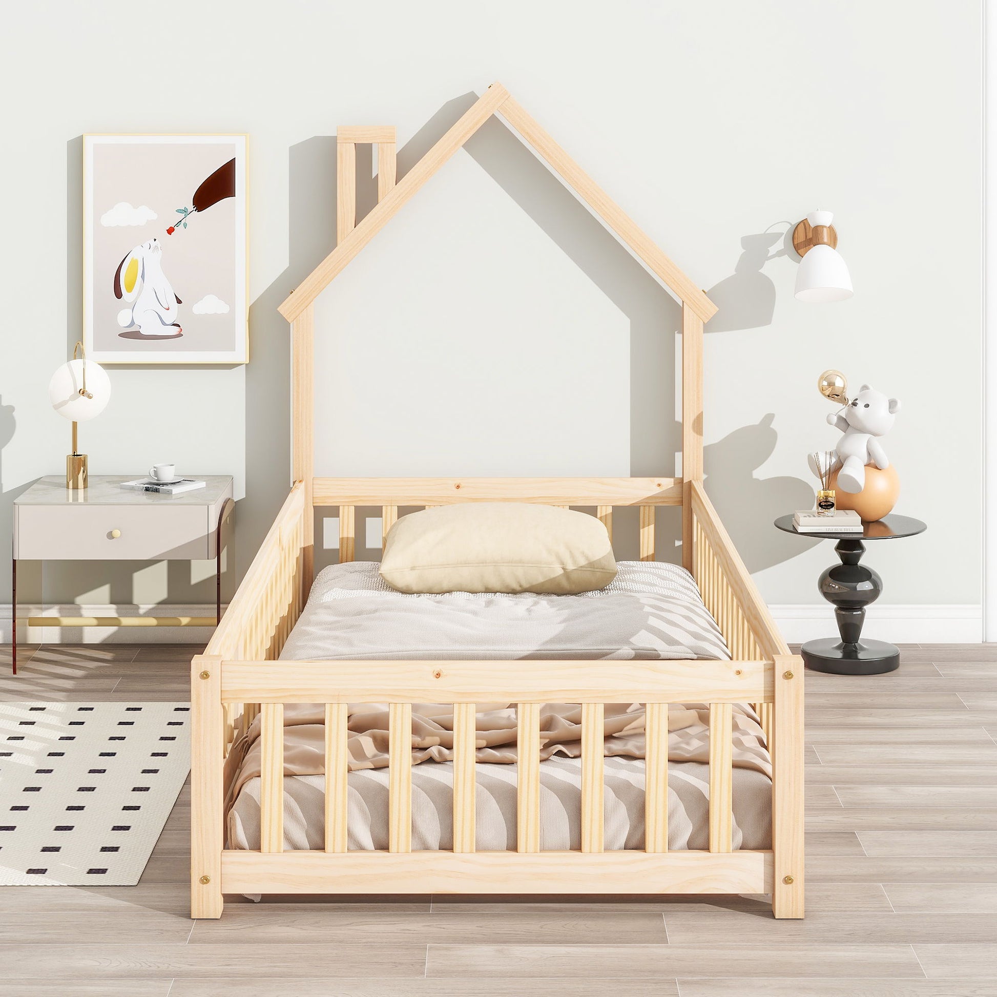 A House-Shaped Headboard Floor Bed With Fence with beige bedding sits in a bright room. To the left is a nightstand with a lamp beneath animal art; on the right, a small table holds a toy under a wall sconce.