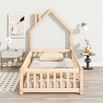 A House-Shaped Headboard Floor Bed With Fence with beige bedding sits in a bright room. To the left is a nightstand with a lamp beneath animal art; on the right, a small table holds a toy under a wall sconce.