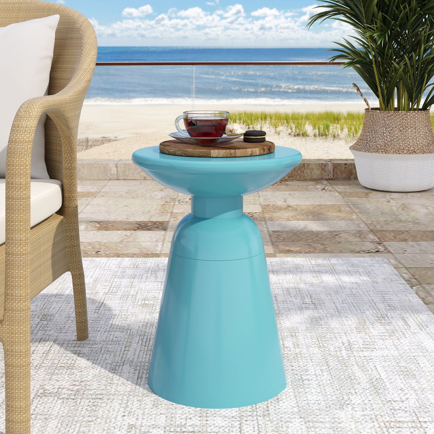 An Outdoor Modern Metal End Large Table on a patio holds a wooden tray with tea and cookies. Nearby are a wicker chair, potted plant, and an ocean view in the background.