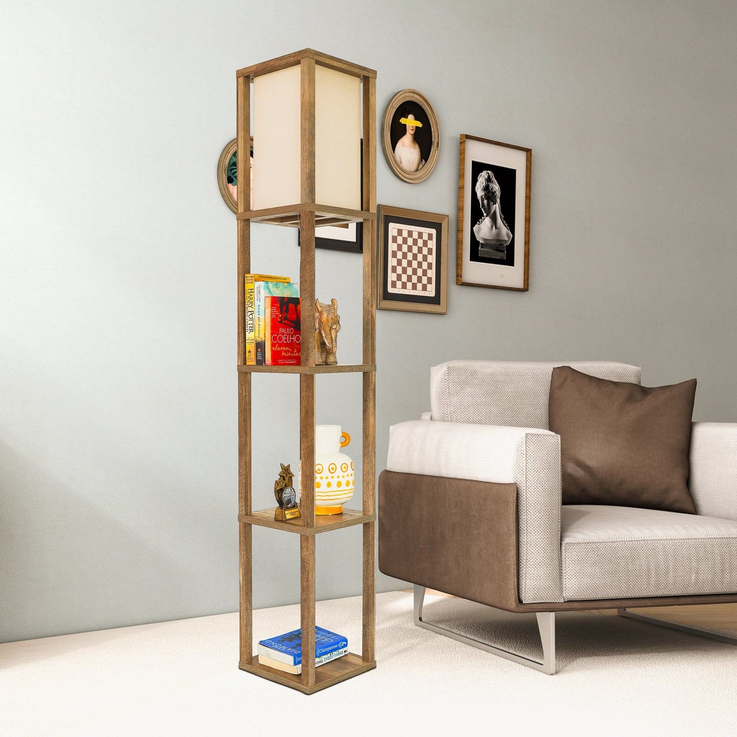 A modern living room with a beige armchair, brown cushion, and the Pinnacle Shelf Floor Lamp in natural wood/white, displaying books and decor. Art and photos hang on the light-colored wall behind the lamp.
