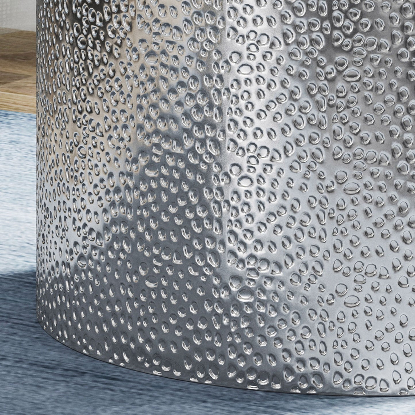 Close-up of the Modern Round Accent Table with a hammered, metallic surface reflecting light, placed on a light blue rug beside a wooden surface.