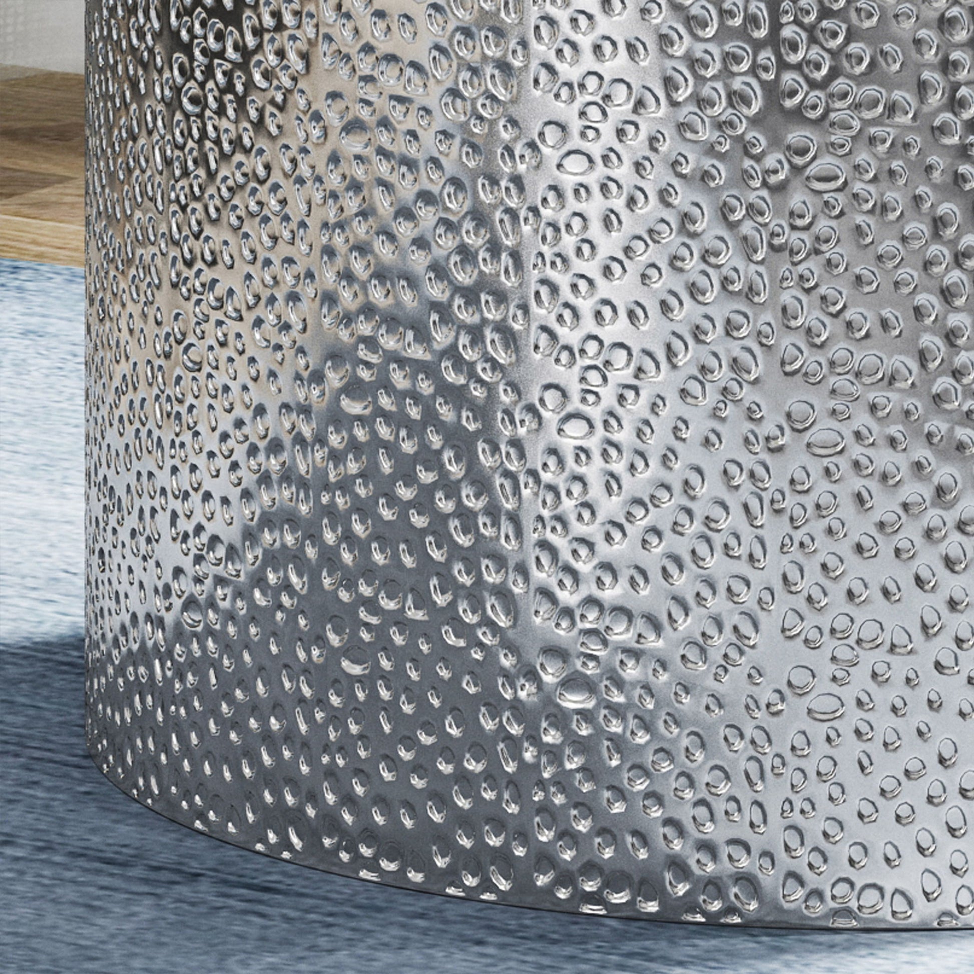 Close-up of the Modern Round Accent Table with a hammered, metallic surface reflecting light, placed on a light blue rug beside a wooden surface.
