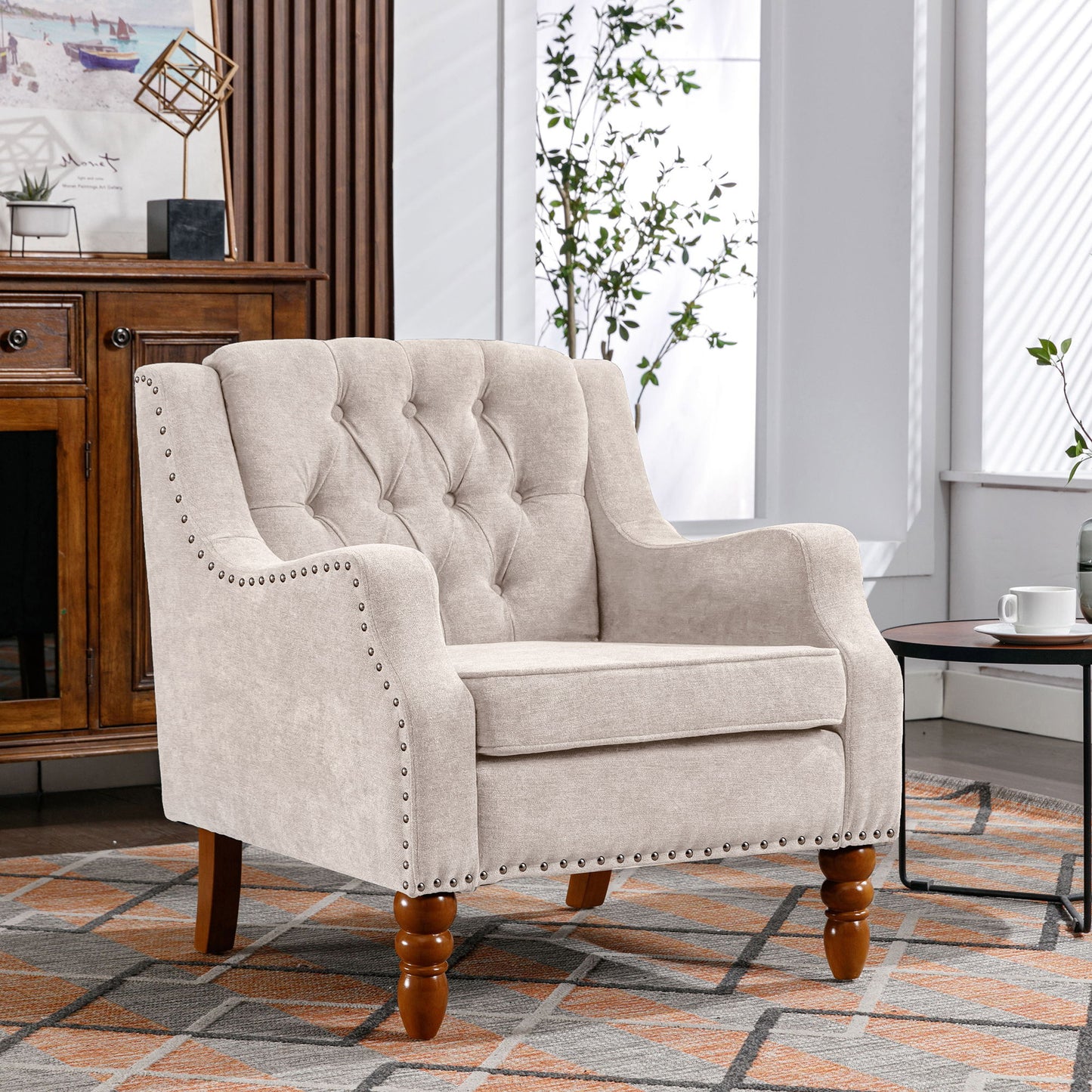 A button-tufted Accent Chair with vintage brass studs and wooden legs sits on a patterned rug in a bright living room, beside a round coffee table and wooden cabinet. Perfect as a comfy reading or reception chair.