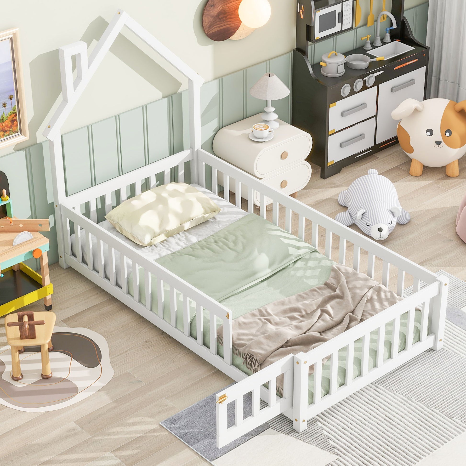 A cozy kids’ bedroom features a House-Shaped Headboard Floor Bed With Fence, pastel bedding, soft pillow, plush bear toy, play kitchen set, nightstand, and wooden toys on a light floor with green-paneled wall.