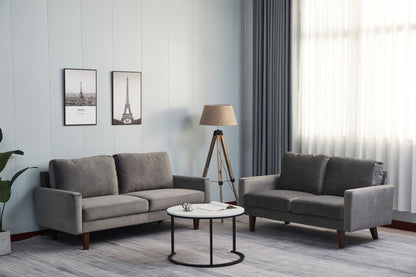 Modern living room featuring two Comfortable Sofas With Durable Construction, a round white coffee table, floor lamp, framed prints on a light wall, and a potted plant in the corner for a minimalist, cozy feel.