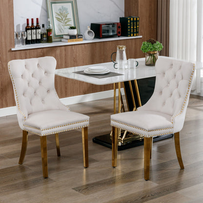 Two Nikki modern tufted velvet dining chairs with golden stainless steel legs and nailhead trim sit on a wooden floor in a contemporary dining room, paired with a marble-top table set for a meal.