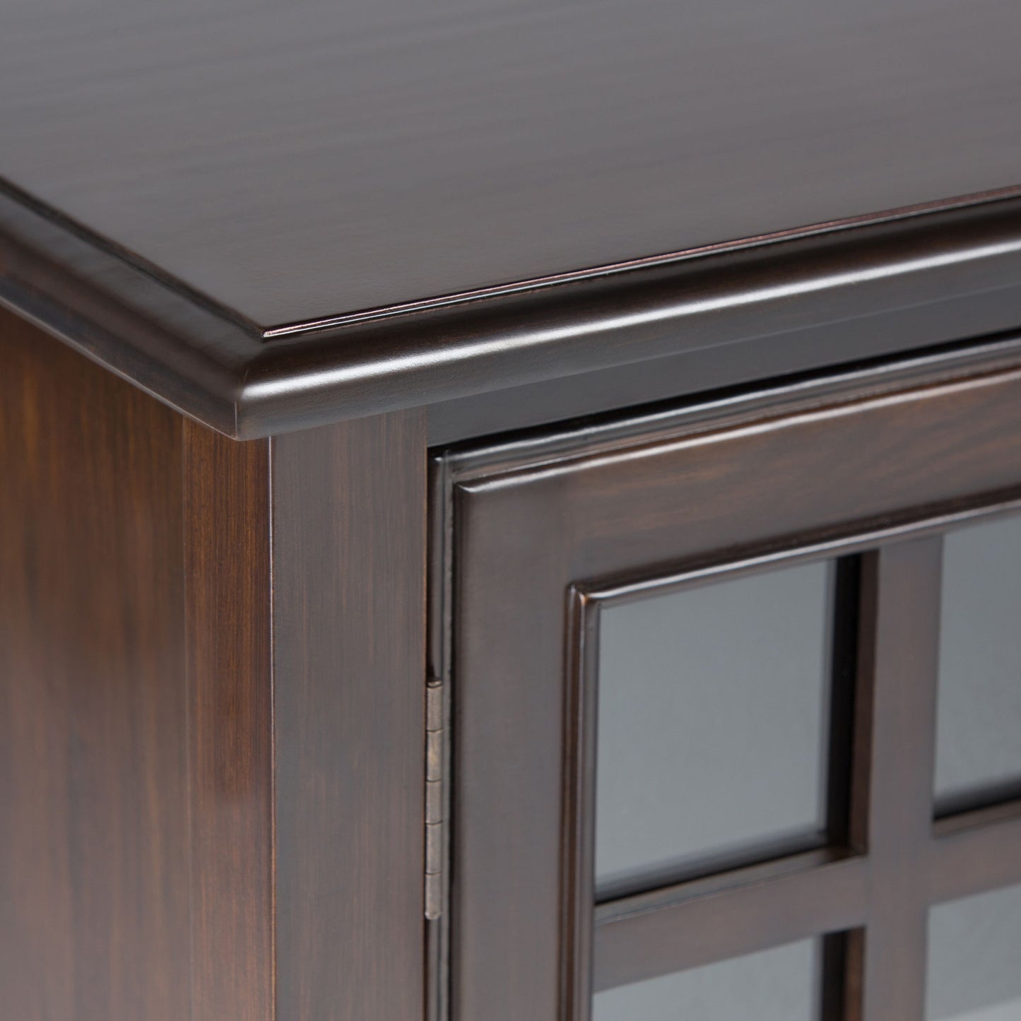 Close-up of the upper corner of the Connaught Tall Storage Cabinet in Dark Chestnut Brown, featuring a glass-paneled door and decorative trim along the top edge.