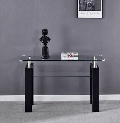 The Clear Glass Top Side Table, Modern Design For Home, with black legs stands against a gray wall. On it sit a small black bust sculpture and two stacked books. A framed Empire State Building photo is mounted above.