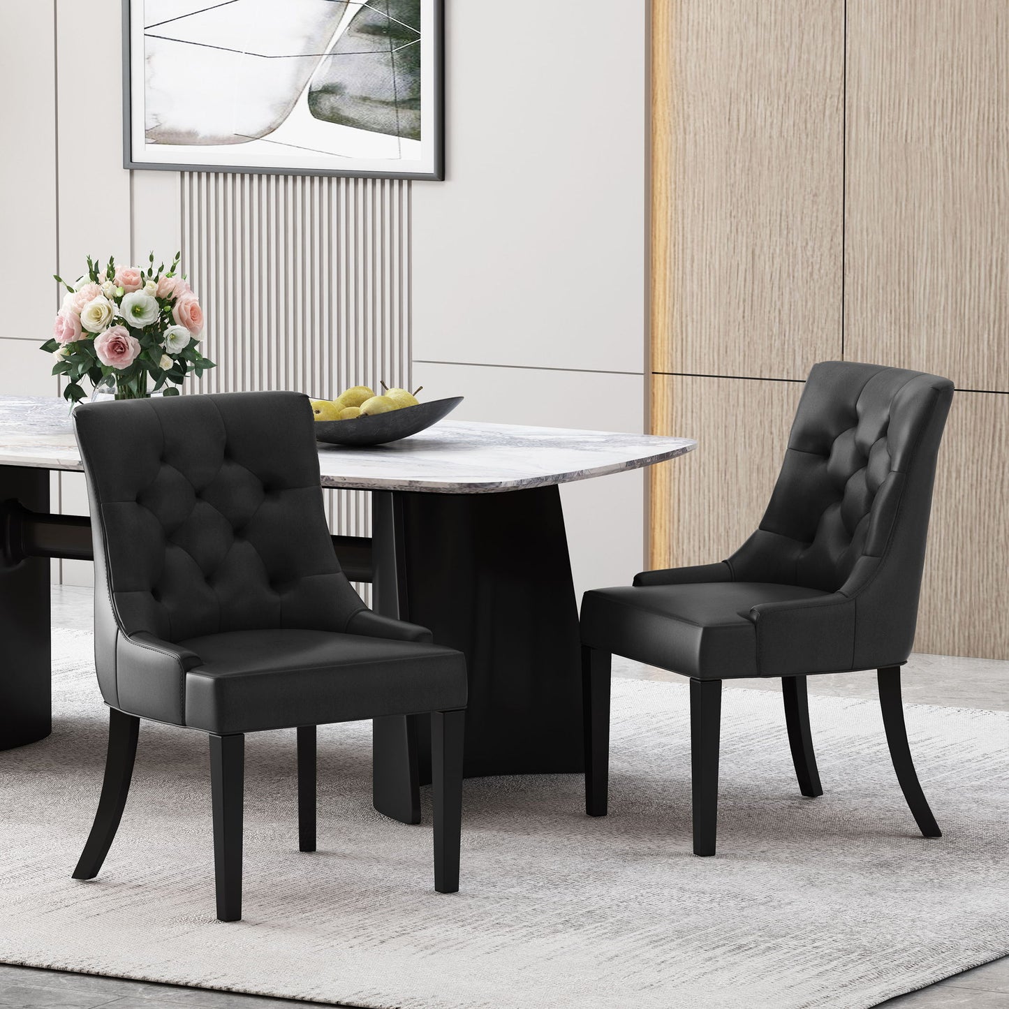 A set of two Cheney Contemporary Dining Chairs with black tufted upholstery sits by a modern marble table with a black base. The table is decorated with a flower vase and lemons, set against wood paneling and framed artwork in the background.