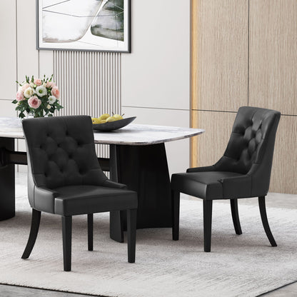 A set of two Cheney Contemporary Dining Chairs with black tufted upholstery sits by a modern marble table with a black base. The table is decorated with a flower vase and lemons, set against wood paneling and framed artwork in the background.