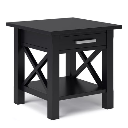 The Kitchener - Handcrafted Table is a black wooden end table featuring a single drawer with a silver handle, X-shaped side supports, and a lower shelf.