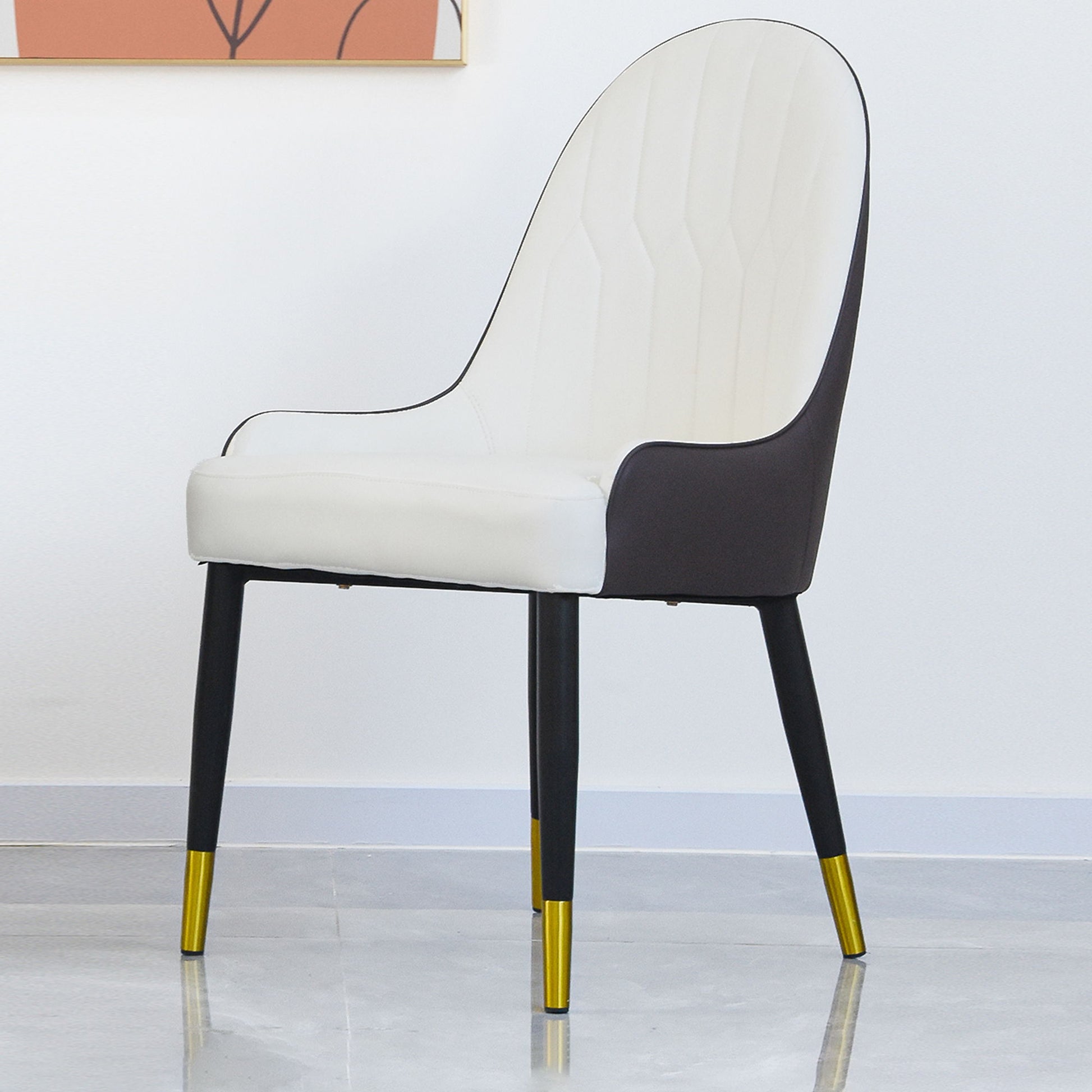 The Modern PU Sponge-Filled Dining Chair (Set of 2) features a white cushioned seat and back, black outer shell and legs with gold tips, perfect for restaurants, living rooms, or rooms. Shown on a light gray floor against a white wall.