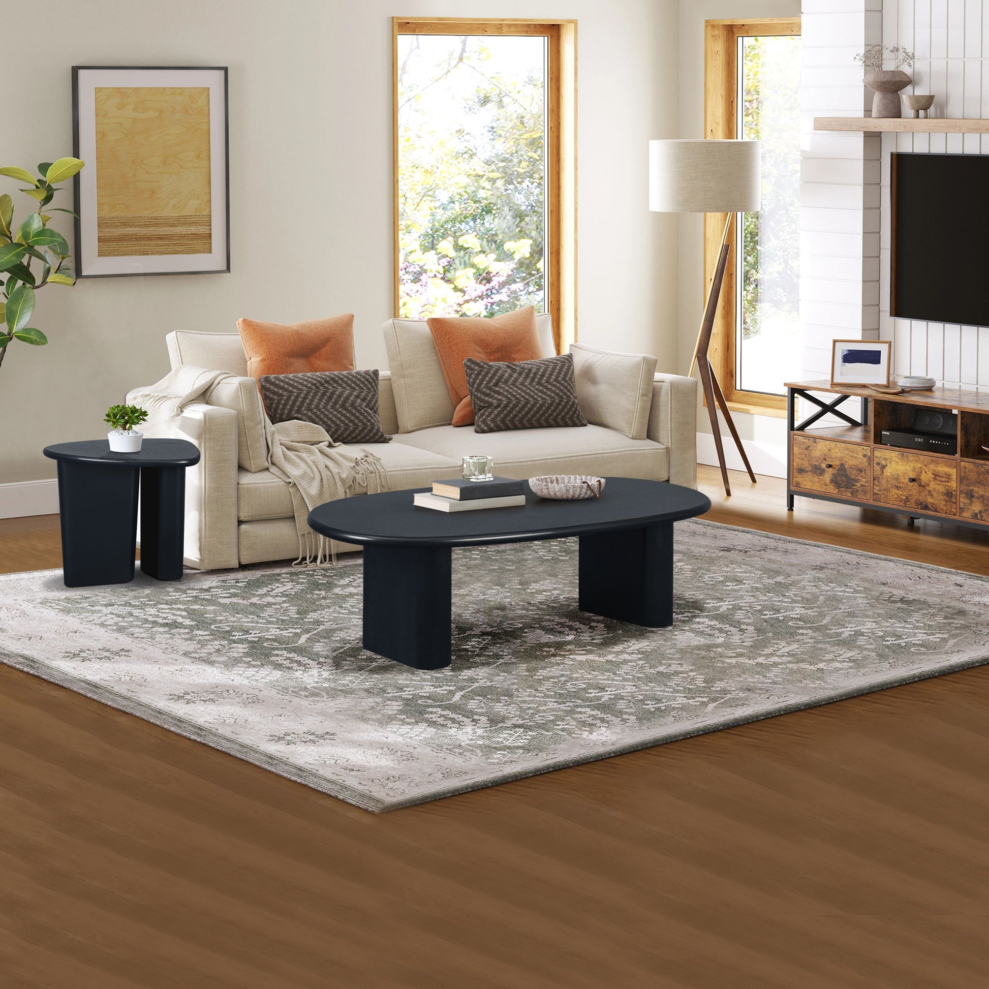 A modern living room with a beige sofa, orange and beige cushions, a Tapered Tabletop Coffee Table in Antique Black, a small side table, floor lamp, patterned rug, and large windows letting in natural light.