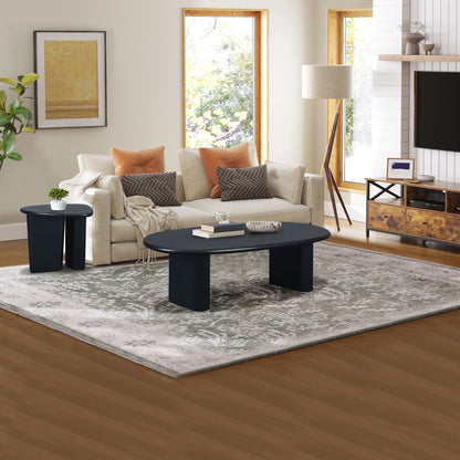 A modern living room with a beige sofa, orange and beige cushions, a Tapered Tabletop Coffee Table in Antique Black, a small side table, floor lamp, patterned rug, and large windows letting in natural light.