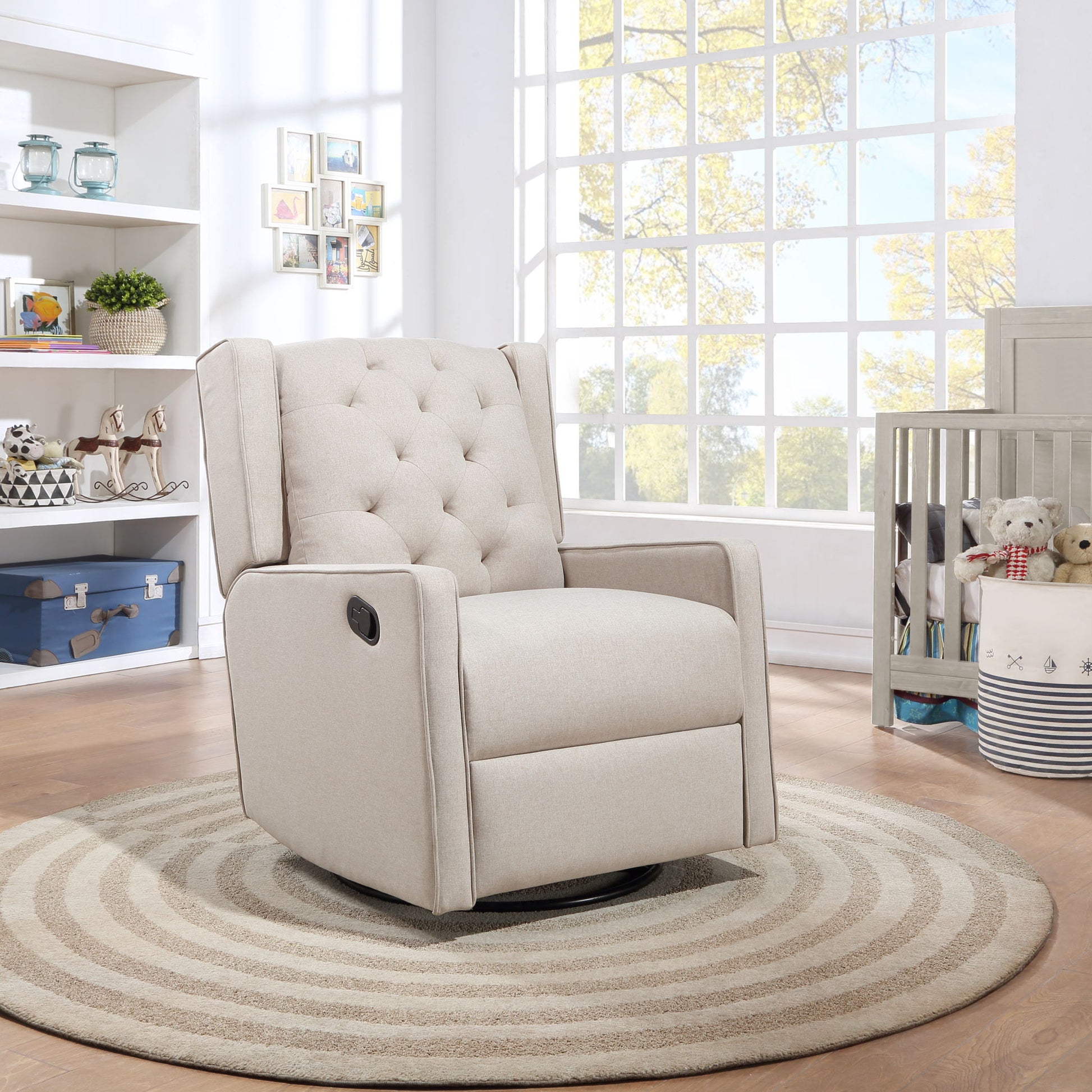 The Milah Gliding Swivel Recliner Tufted in beige rests on a circular striped rug in a sunny nursery with large windows, shelves filled with toys and books, and a crib with stuffed animals. Sunlight streams through the windows.