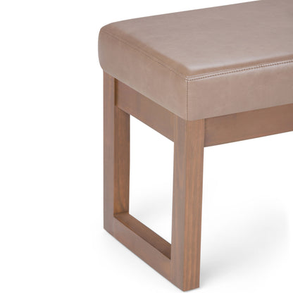 A close-up of the Milltown - Upholstered Ottoman Bench, showcasing its light brown cushioned seat with stitched edges and a rectangular wooden base with a geometric, open-sided design.