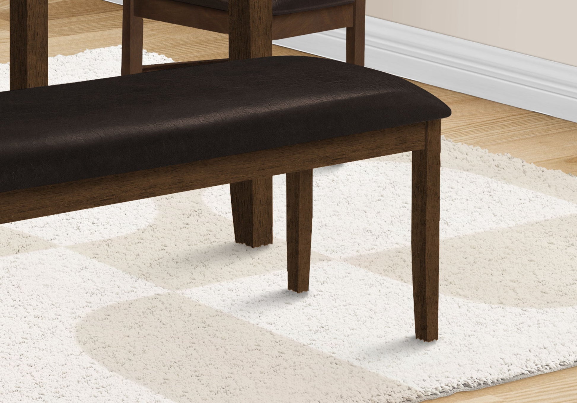 A close-up of a Rectangular Upholstered Bench in a transitional style sits on a cream and white patterned rug, with part of a matching chair and hardwood floor in the background.